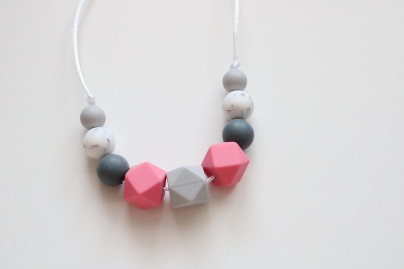 May include: A pink and gray silicone necklace with geometric beads. The necklace is made of a soft, flexible material and is perfect for teething babies.