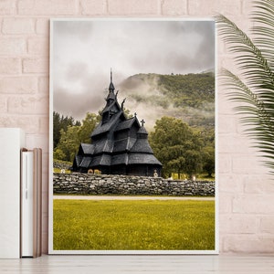 Puede incluir: Una iglesia de madera negra con un techo empinado y múltiples torres se alza en un campo de hierba. La iglesia está rodeada por un muro de piedra y árboles. El fondo presenta una ladera montañosa brumosa.