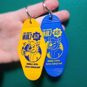 May include: Two keychains, one yellow and one blue, with a retro motel key design. Each keychain features the text "VAULT 621" and a cartoon character. The yellow keychain has the text "Building a better Furture underground!"