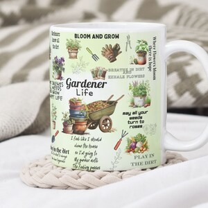 May include: White ceramic mug with a green background and colorful illustrations of gardening tools, plants, and flowers. The text "Gardener Life" is printed in black on the mug. Other text includes "Bloom and Grow", "Breathe in dirt and exhale flowers", "May all your weeds turn to roses", and "Play in the dirt".