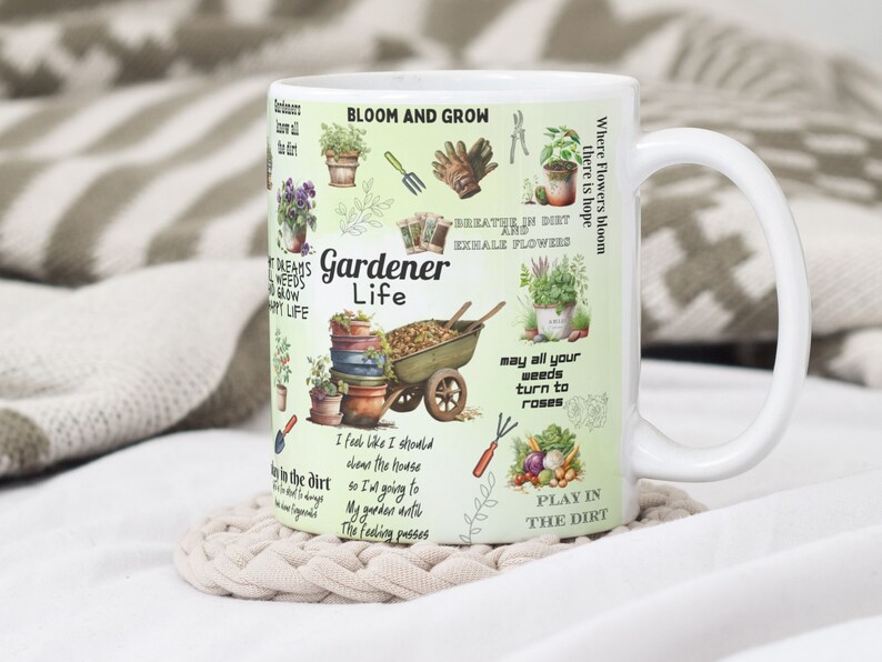 May include: White ceramic mug with a green background and colorful illustrations of gardening tools, plants, and flowers. The text "Gardener Life" is printed in black on the mug. Other text includes "Bloom and Grow", "Breathe in dirt and exhale flowers", "May all your weeds turn to roses", and "Play in the dirt".