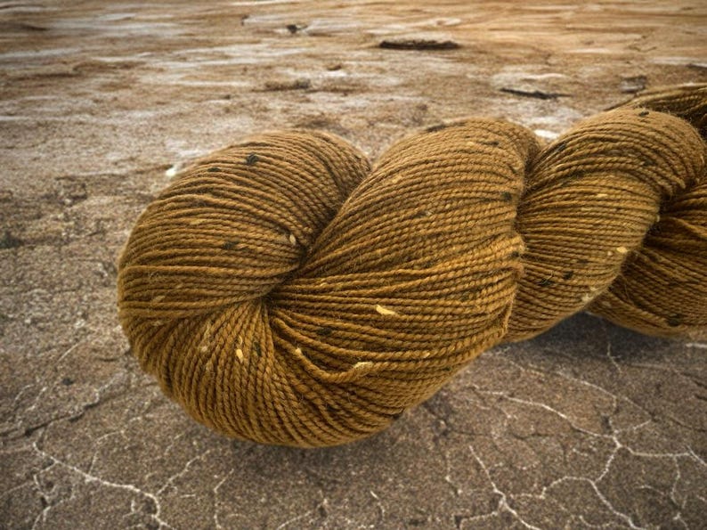 May include: A skein of brown yarn with flecks of black and white. The yarn is twisted and has a textured appearance.