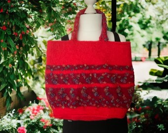 May include: A vibrant red tote bag with a textured knit design. The bag features decorative bands of embroidered floral patterns in shades of purple, blue, and brown. The handles are also red and knitted.