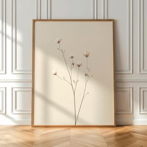 May include: A framed botanical print showing a sprig of white flowers on a cream background. The artwork is in a warm-toned wooden frame, creating a minimalist and natural aesthetic. The print is displayed against a white wall and wooden floor.