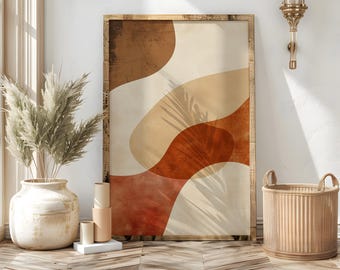 May include: Abstract art print in a wooden frame. The artwork features overlapping organic shapes in shades of brown, beige, and rust. The print is displayed in a room with a vase of dried plants, decorative cylinders, and a woven basket.