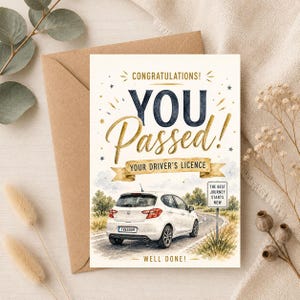 Op de afbeelding: Een wenskaart met een witte hatchback op een weg met een bord waarop staat THE BEST JOURNEY STARTS NOW. De tekst luidt CONGRATULATIONS! YOU Passed! YOUR DRIVER'S LICENCE en WELL DONE! Het kenteken van de auto bevat de tekst FREEDOM.
