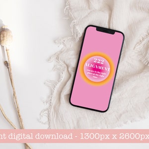 May include: A pink phone screen with a yellow and orange circle that says "222 Alignment you are in the right place at the right time". The phone is lying on a white fabric surface.