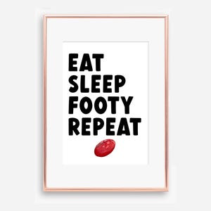Puede incluir: Impresión enmarcada con las palabras "EAT SLEEP FOOTY REPEAT" en letras negras en negrita. Un balón de fútbol rojo está en la parte inferior. El marco es de color oro rosa.