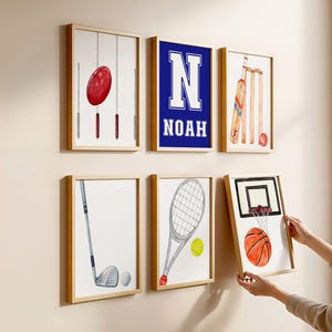 May include: A collection of framed watercolor art prints featuring sports equipment. The prints include a football, a cricket set, a golf club and ball, a tennis racket and ball, and a basketball hoop and ball. One print has the letter "N" and the name "NOAH".