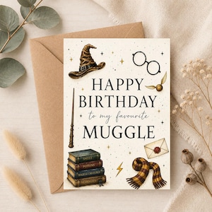 May include: A cream-coloured greeting card with the text "HAPPY BIRTHDAY to my favourite MUGGLE" surrounded by illustrations of a brown wizard hat, round glasses, a wand, a stack of four books, a golden snitch, a letter, and a striped scarf.