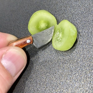 Op de afbeelding: Een klein mes met een houten handvat en een damaststalen blad wordt gebruikt om een ​​groene druif doormidden te snijden.