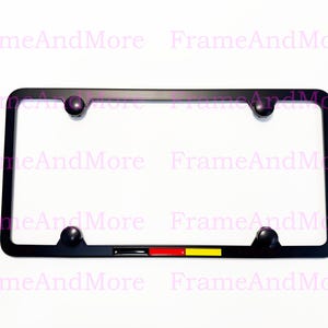 May include: Black license plate frame with four black screw caps. The frame has a small German flag design in the lower right corner. The text "FrameAndMore" is repeated in pink across the image.