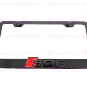 May include: Black license plate frame with the letters "SQ5" in black and red. The frame has two black screw caps at the top. The frame is designed to fit a standard U.S. license plate.