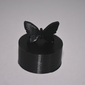 Peut inclure: Une figurine de papillon noire imprimée en 3D sur une base circulaire noire.