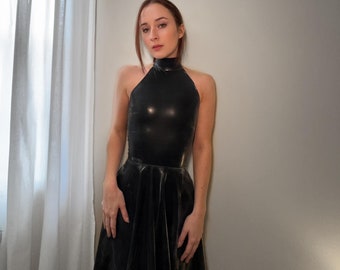 May include: A woman wearing a black halter top and a black skirt. She is standing in front of a white wall.