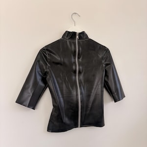 May include: A black, shiny, short-sleeved top with a high mock neck collar. The garment features a full-length silver-toned metal zip running vertically down the centre front, extending from the collar to the bottom hem of the shirt.