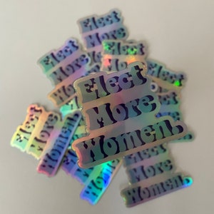 Può includere: Un mucchio di adesivi olografici iridescenti con il testo "Elect More Women" in lettere nere.