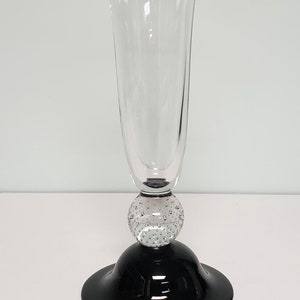May include: A clear glass vase with a black base and a textured glass ball in the middle. The vase has a wide opening and a narrow neck.