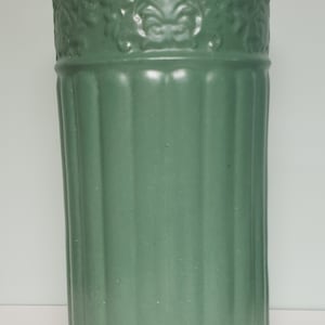 Może przedstawiać: Zielona ceramiczna doniczka z żebrowanym wzorem i ozdobnym tłoczonym wzorem wokół górnej krawędzi.