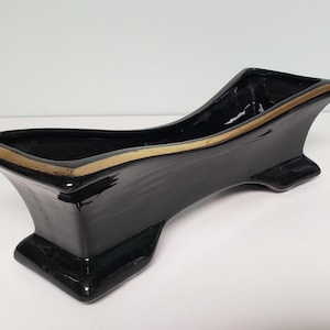 May include: Black ceramic planter with a gold rim. The planter is shaped like a long, narrow boat and has a slightly curved bottom.