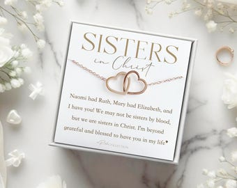 May include: A white card with the text "Sisters in Christ" and a rose gold necklace with two intertwined hearts. The card reads "Naomi had Ruth, Mary had Elizabeth, and I have you! We may not be sisters by blood, but we are sisters in Christ. I'm beyond grateful and blessed to have you in my life."