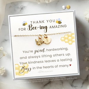May include: A white card with gold lettering that reads "Thank you for Bee-ing Amazing". The card features a gold bee charm necklace with a letter "S" charm. The card also has a honeycomb design and the text "You're sweet, hardworking, and always lifting others up. Your kindness leaves a lasting Buzz in the hearts of many."
