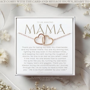 May include: A white card with the words "To an Amazing Mama" in gold lettering. The card has a message about being a rock, cheerleader, and forever friend. A gold necklace with two intertwined heart charms is displayed on the card.