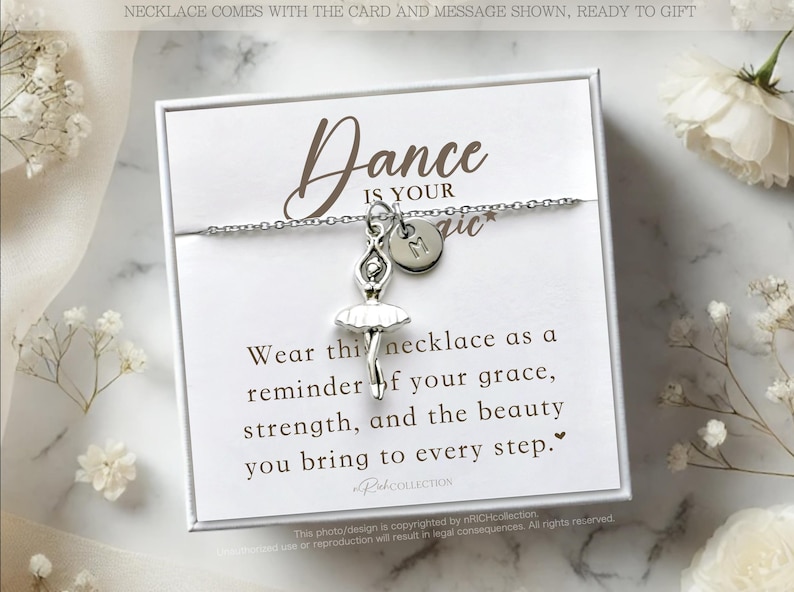 May include: A white card with a silver necklace featuring a ballerina charm and a letter charm. The card reads "Dance is your magic" and includes a message about grace, strength, and beauty.