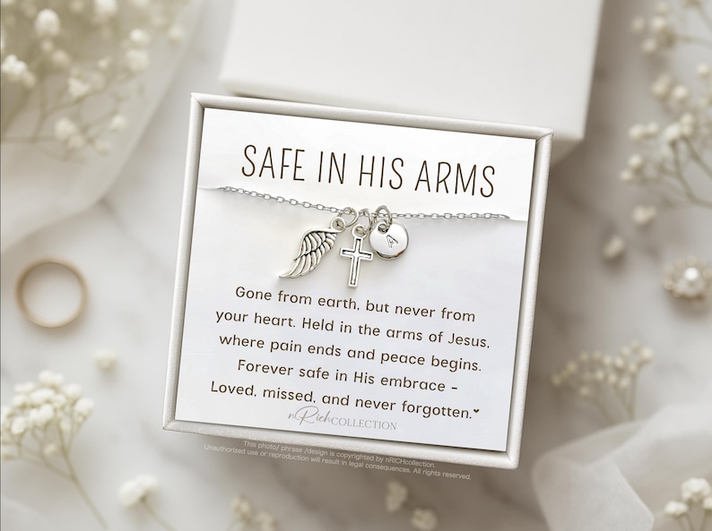 May include: A silver necklace with a cross, angel wing, and heart charm. The necklace comes in a white box with a message that reads "Safe in His Arms. Gone from earth, but never from your heart. Held in the arms of Jesus, where pain ends and peace begins. Forever safe in His embrace - Loved, missed, and never forgotten."