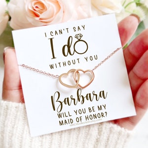 Peut inclure: Une carte blanche avec le texte "Je ne peux pas dire oui sans toi" et "Veux-tu &ecirc;tre ma demoiselle d'honneur ?" avec un collier en or rose avec deux c&oelig;urs entrelac&eacute;s. La carte comprend &eacute;galement le nom "Barbara" et le site Web "nRICHcollection.etsy.com".