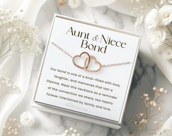 May include: A white card with the text "Aunt & Niece Bond" and a message about the bond between an aunt and niece. The card is next to a rose gold necklace with two intertwined hearts.