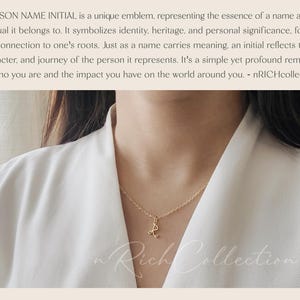 Op de afbeelding: Een gouden ketting met een delicaat initiaal sieraad. De ketting wordt gedragen door een persoon met lang donker haar. De achtergrond is een wit oppervlak.
