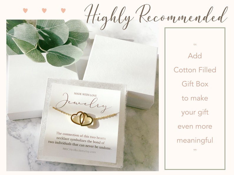 May include: A gold necklace with two interlocking hearts, presented in a white gift box with a white background. The box is decorated with a small card that reads "Made with Love, Jewelry". The card also includes a description of the necklace and the website address "noCHcollection.etsy.com".