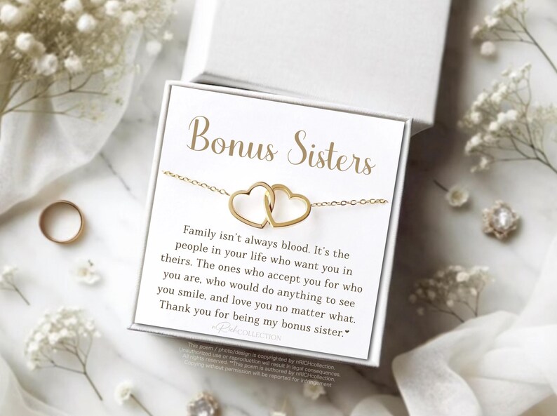 May include: A gold-colored necklace with two connected heart pendants, presented in a white gift box. The box features the words "Bonus Sisters" in gold lettering, along with a heartfelt message. The background includes floral accents.