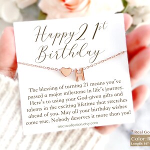 May include: A rose gold necklace with a heart and the letter H charm. The necklace comes with a card that says "Happy 21st Birthday" and includes a message about the blessing of turning 21. The card also says "Real Gold Plated" and "Color: Rose Gold" and "Length: 16" + 3" extension".