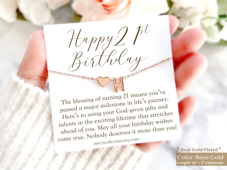 May include: A rose gold necklace with a heart and the letter H charm. The necklace comes with a card that says "Happy 21st Birthday" and includes a message about the blessing of turning 21. The card also says "Real Gold Plated" and "Color: Rose Gold" and "Length: 16" + 3" extension".