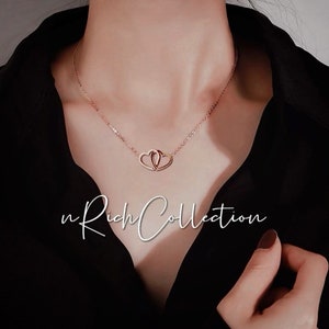 May include: Rose gold necklace featuring two intertwined heart pendants. The delicate chain and pendants are a warm, metallic color. The text "n Rich Collection" is displayed in a cursive font.