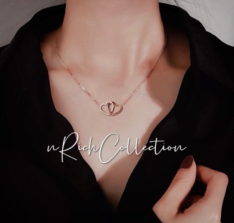 May include: Rose gold necklace featuring two intertwined heart pendants. The delicate chain and pendants are a warm, metallic color. The text "n Rich Collection" is displayed in a cursive font.
