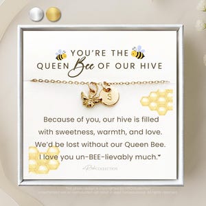 May include: A gold-colored necklace with a bee charm and a round initial pendant, presented in a white gift box. The box features the text "You're the Queen Bee of our Hive" and a message about love and appreciation.