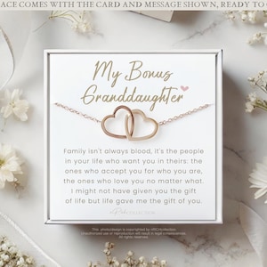 May include: A white card with the text "My Bonus Granddaughter" and a message about family. The card is next to a gold necklace with two interlocking heart charms.