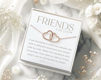 Peut inclure: Une boîte cadeau blanche contenant un collier en or avec deux cœurs entrelacés. La boîte porte le message "FRIENDS FOR LIFE" et "La vraie amitié, c'est quand deux personnes peuvent aller dans des directions différentes mais rester côte à côte. Portez ce collier et souvenez-vous que côte à côte ou à des kilomètres de distance, nos cœurs sont liés."