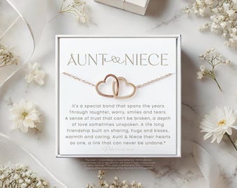 May include: A rose gold necklace with two interlocking heart pendants, presented on a white card with the words "Aunt & Niece". The card includes a poem about the special bond between an aunt and niece. The image is decorated with white flowers.