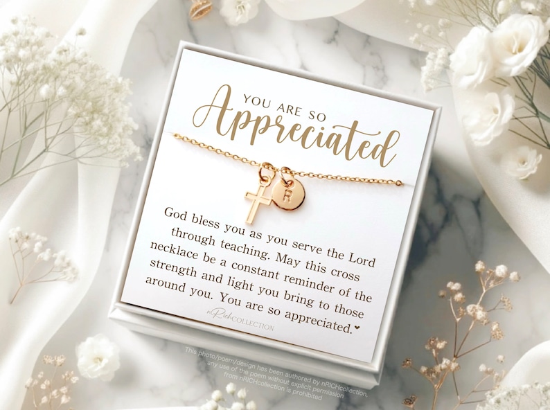 May include: A white gift box with a gold necklace inside. The necklace has a small cross charm and a round charm with the letter "R" on it. The box has a message that reads "You are so appreciated. God bless you as you serve the Lord through teaching. May this cross necklace be a constant reminder of the strength and light you bring to those around you. You are so appreciated."
