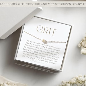 Op de afbeelding: Een witte cadeaudoos met een witte kaart erin. De kaart heeft een gouden ketting met een parelbedel en de tekst "GRIT" en een boodschap over de kracht en veerkracht van een parel.