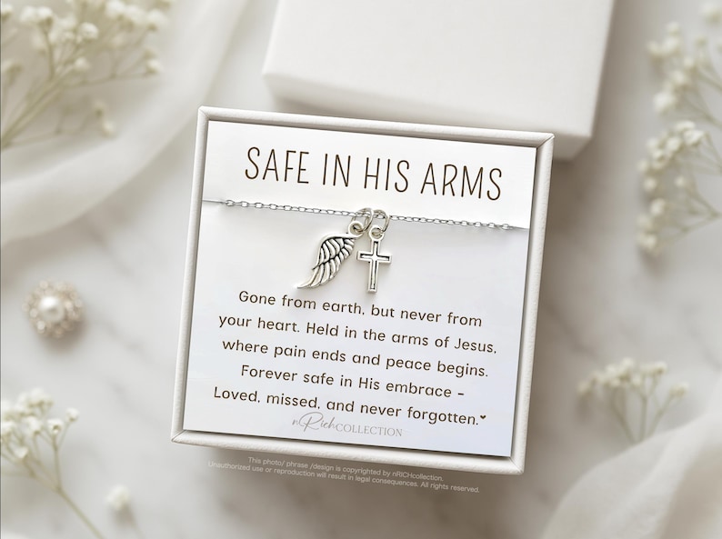 May include: A white card with the text "SAFE IN HIS ARMS" and a silver necklace with a cross and angel wing charm. The card reads "Gone from earth, but never from your heart. Held in the arms of Jesus. Where pain ends and peace begins. Forever safe in His embrace - Loved, missed, and never forgotten."