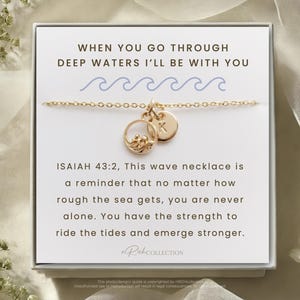 May include: Gold wave necklace with a small charm that says "K". The necklace comes in a white box with the text "WHEN YOU GO THROUGH DEEP WATERS I'LL BE WITH YOU" and "ISAIAH 43:2, This wave necklace is a reminder that no matter how rough the sea gets, you are never alone. You have the strength to ride the tides and emerge stronger."