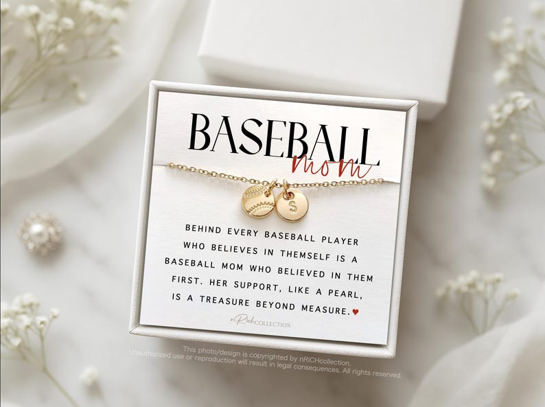 May include: A white box with a gold necklace featuring a baseball charm and a letter charm. The box has the text "BASEBALL mom" and a quote about the importance of a baseball mom's support.