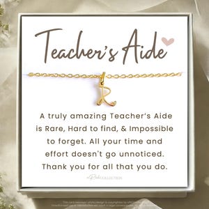 May include: A white card with a gold chain necklace and a small gold letter "R" charm. The card reads "Teacher's Aide" and includes a message thanking a teacher's aide for their hard work.