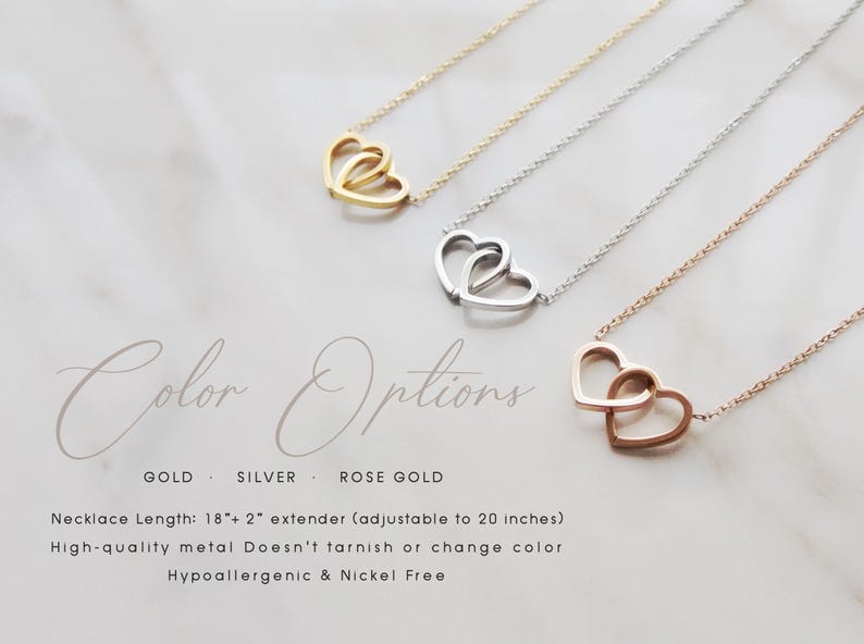 May include: Necklaces with interlocking heart pendants in gold, silver, and rose gold. The necklaces are displayed on a marble surface. The text "Color Options" is above the necklaces. The text below the necklaces reads "GOLD SILVER ROSE GOLD".