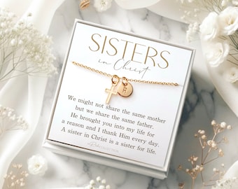 May include: A white gift box with a gold necklace inside. The necklace has a small cross charm and a letter charm. The box has a card that reads "Sisters in Christ" and a message about the bond between sisters.